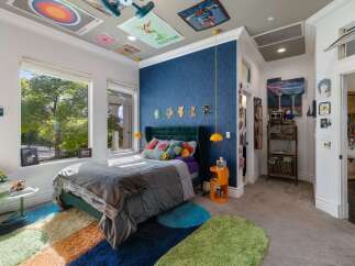 This vibrant bedroom features a plush green velvet headboard and a large window offering serene views of lush greenery.