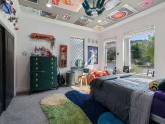 This eclectic bedroom features a vibrant green dresser adorned with gold hardware, complemented by a collection of colorful rugs on the floor.
