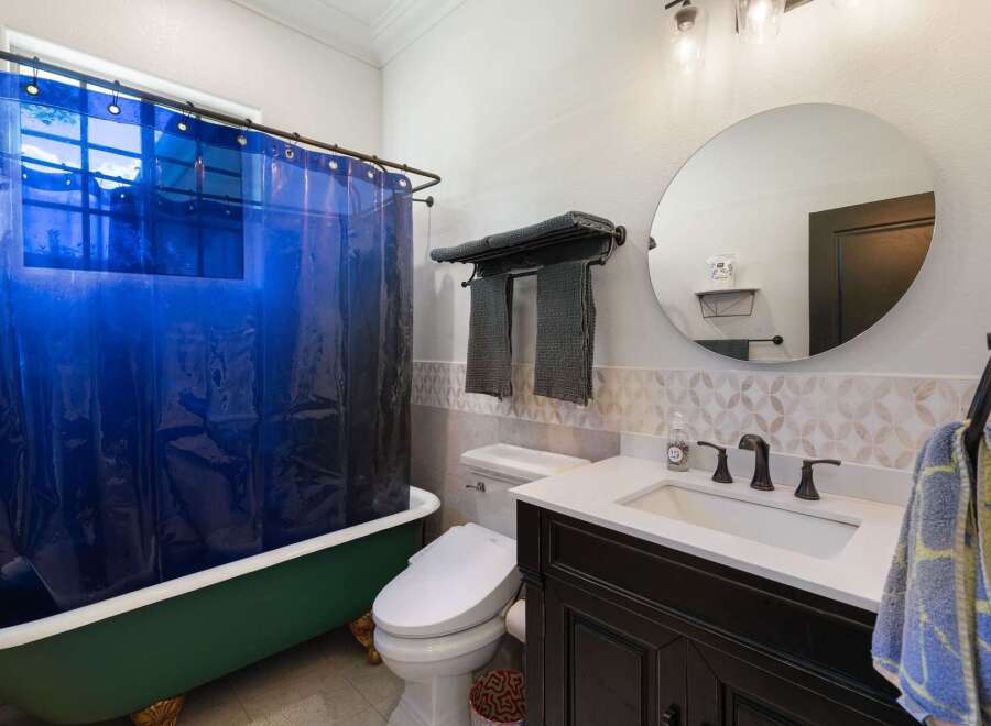 This charming bathroom features a vibrant green clawfoot bathtub paired with a striking blue shower curtain, creating a unique focal point.