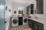This spacious laundry room features modern dark cabinetry with elegant gold hardware, complemented by a sleek white countertop and a deep sink.