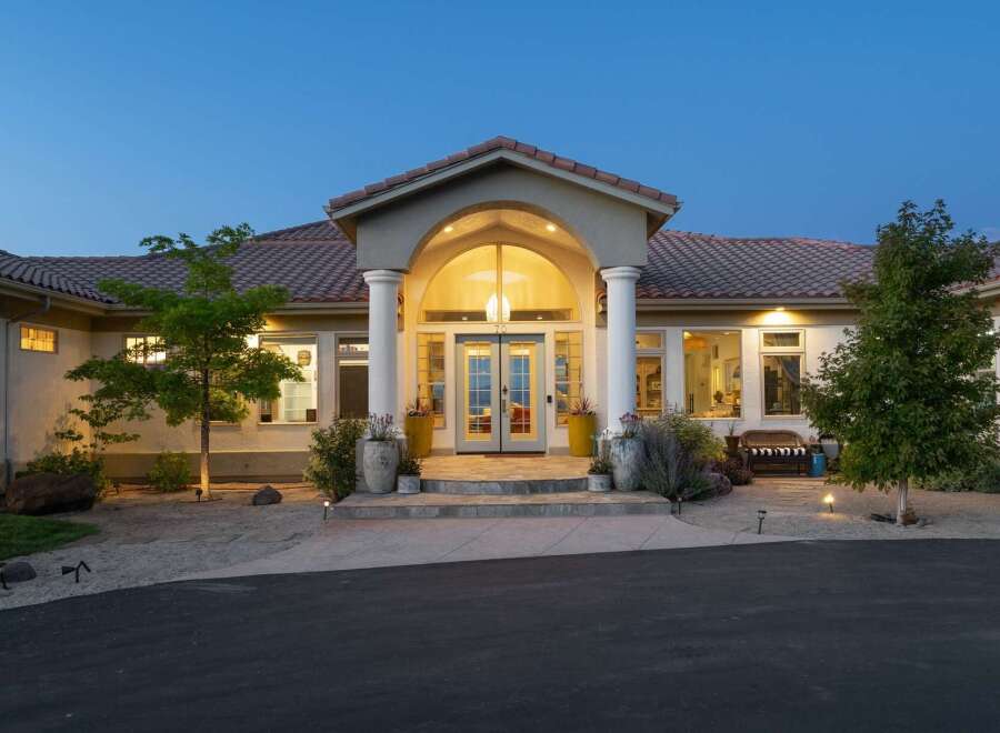 This stunning residence features a grand arched entryway with elegant columns, leading to double doors and large windows that illuminate the interior.