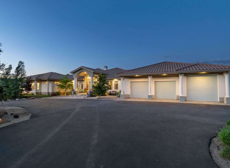This stunning estate features a grand entrance with arched columns and a spacious driveway leading to a multi-car garage.