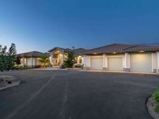 This stunning estate features a grand entrance with arched columns and a spacious driveway leading to a multi-car garage.