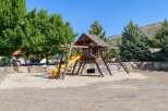 This property features a fantastic wooden playground with a yellow slide, climbing wall, and swings, perfect for family fun.
