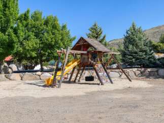 This property features a fantastic wooden playground with a yellow slide, climbing wall, and swings, perfect for family fun.