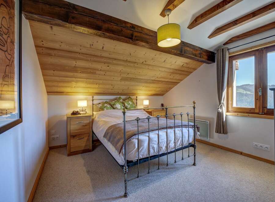Experience cozy mountain living in this charming attic bedroom, featuring a rustic wooden ceiling and exposed beams.