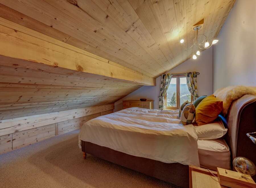 Experience cozy mountain living in this charming attic bedroom, featuring a sloped wooden ceiling and built-in storage.