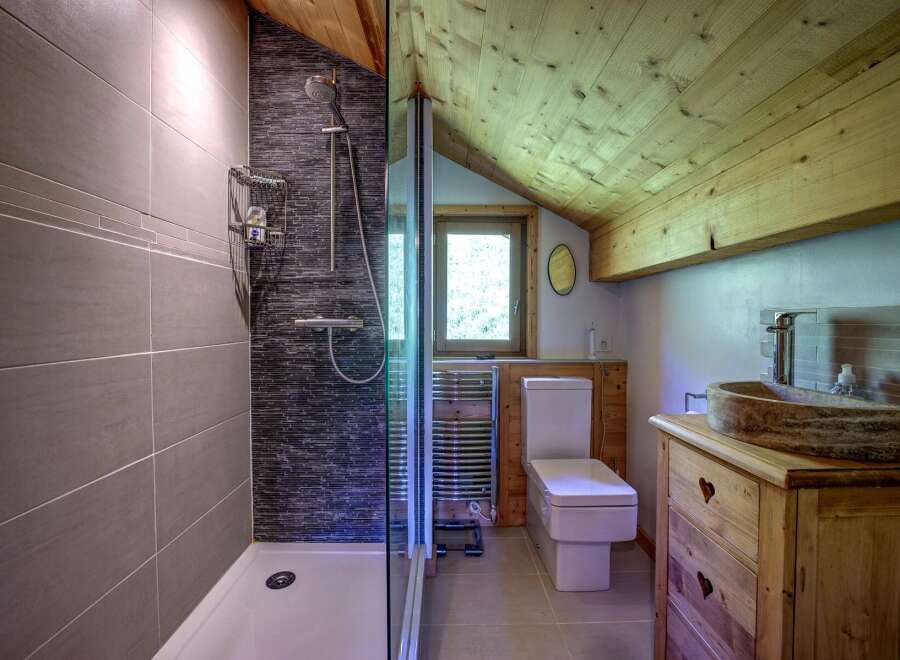 Experience rustic charm in this bathroom featuring a modern walk-in shower with sleek grey tiling and a dark mosaic accent wall.