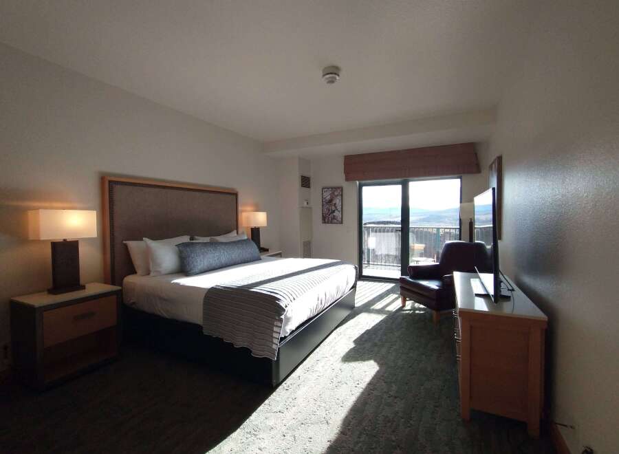 Experience comfort and stunning views in this hotel room, featuring a plush king-sized bed and a private balcony overlooking a scenic landscape.