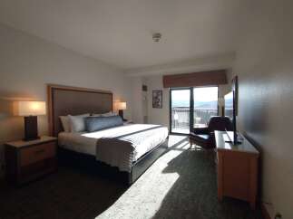 Experience comfort and stunning views in this hotel room, featuring a plush king-sized bed and a private balcony overlooking a scenic landscape.