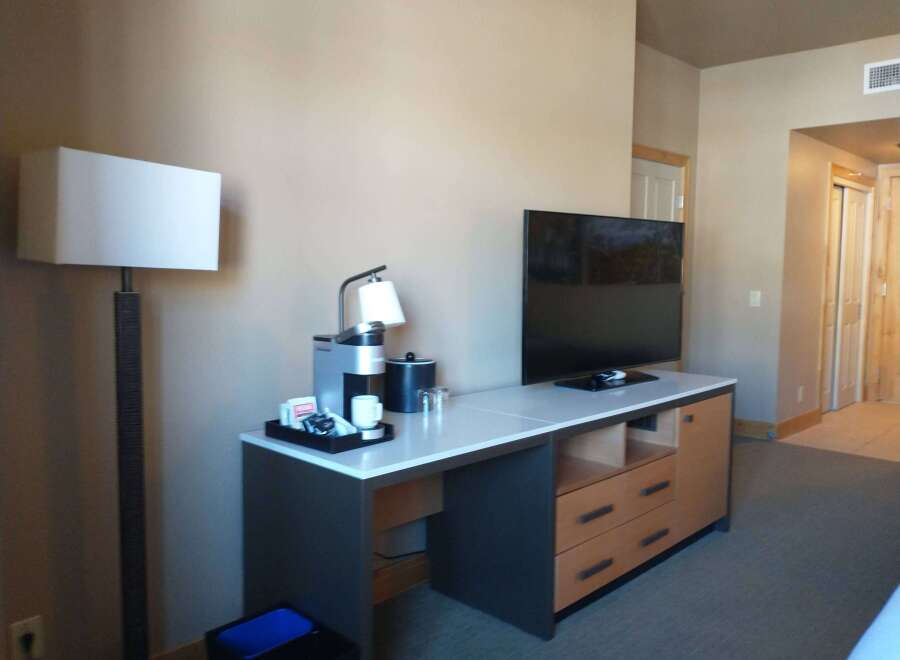 This hotel room features a modern desk area with a coffee maker, mini-fridge, and a flat-screen TV.