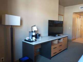 This hotel room features a modern desk area with a coffee maker, mini-fridge, and a flat-screen TV.