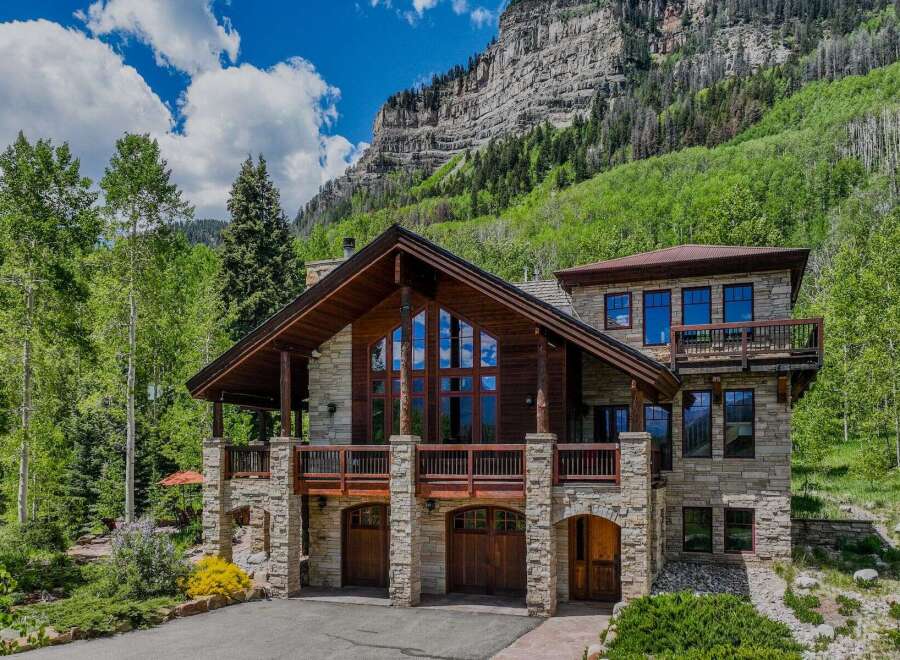 Experience luxury mountain living in this stunning stone and timber home, nestled against a dramatic cliff face and surrounded by lush greenery.