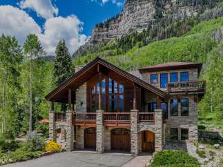 Experience luxury mountain living in this stunning stone and timber home, nestled against a dramatic cliff face and surrounded by lush greenery.