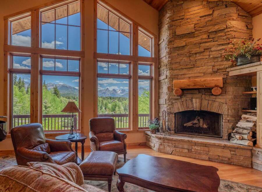 Experience breathtaking mountain views from this stunning living room, featuring a grand stone fireplace and expansive windows.