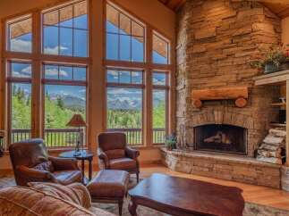 Experience breathtaking mountain views from this stunning living room, featuring a grand stone fireplace and expansive windows.