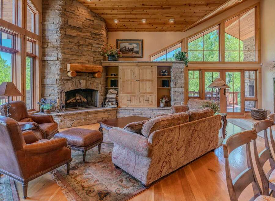 Experience rustic elegance in this stunning living room, featuring a grand stone fireplace and soaring vaulted ceilings with exposed wood beams.