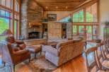Experience rustic elegance in this stunning living room, featuring a grand stone fireplace and soaring vaulted ceilings with exposed wood beams.