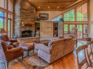Experience rustic elegance in this stunning living room, featuring a grand stone fireplace and soaring vaulted ceilings with exposed wood beams.