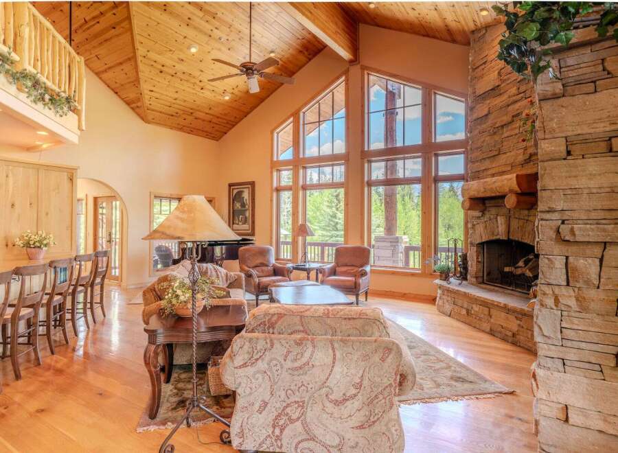 Experience rustic elegance in this stunning living room, featuring a grand stone fireplace and soaring vaulted ceilings with exposed wood beams.