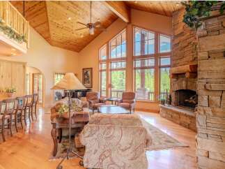 Experience rustic elegance in this stunning living room, featuring a grand stone fireplace and soaring vaulted ceilings with exposed wood beams.