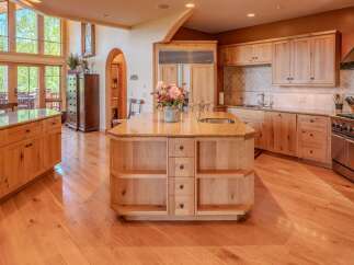 Experience luxury in this stunning kitchen featuring custom light wood cabinetry and a large granite-topped island with a built-in sink.