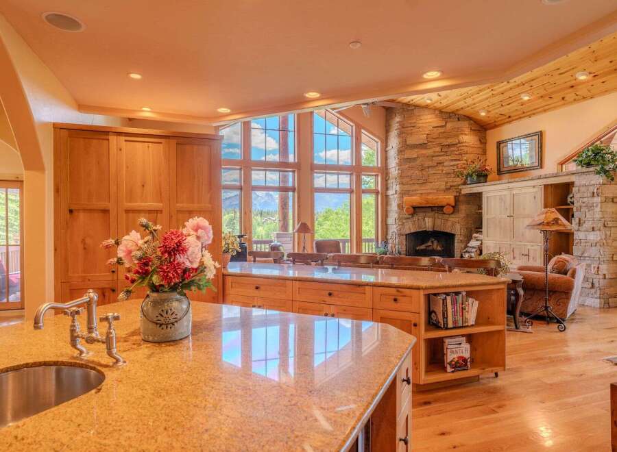 Experience breathtaking mountain views from this stunning kitchen, featuring a large granite island with a sink and faucet, complemented by custom wood cabinetry.