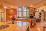 Experience breathtaking mountain views from this stunning kitchen, featuring a large granite island with a sink and faucet, complemented by custom wood cabinetry.