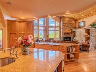 Experience breathtaking mountain views from this stunning kitchen, featuring a large granite island with a sink and faucet, complemented by custom wood cabinetry.
