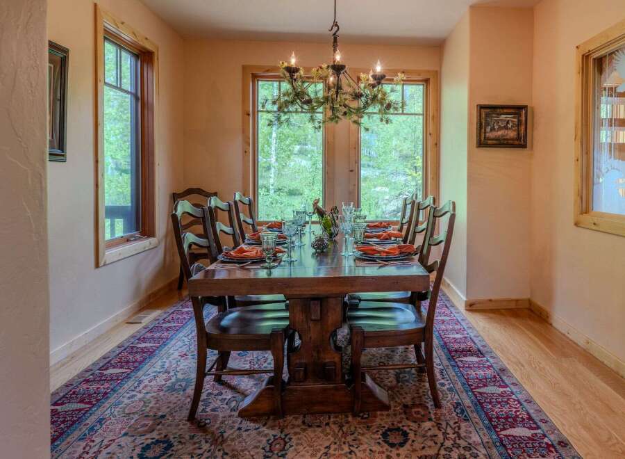 Experience elegant dining in this beautifully appointed dining room, featuring a large wooden table set for ten with vibrant orange napkins and clear glassware.