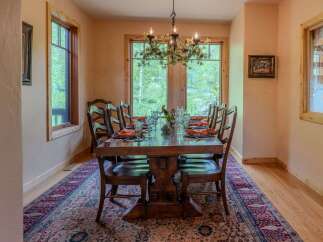 Experience elegant dining in this beautifully appointed dining room, featuring a large wooden table set for ten with vibrant orange napkins and clear glassware.