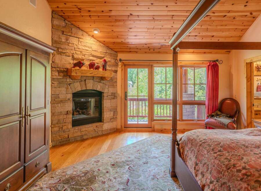 Experience rustic charm in this inviting bedroom featuring a stunning stone fireplace and a natural wood ceiling.