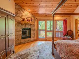 Experience rustic charm in this inviting bedroom featuring a stunning stone fireplace and a natural wood ceiling.