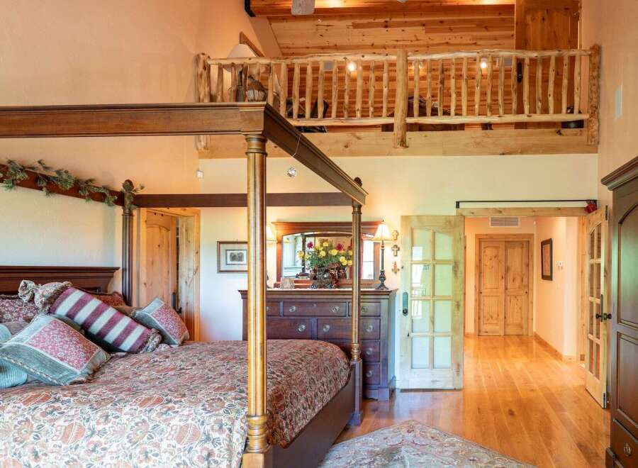 Experience rustic charm in this spacious bedroom featuring a grand four-poster bed adorned with decorative pillows and a cozy comforter.