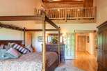 Experience rustic charm in this spacious bedroom featuring a grand four-poster bed adorned with decorative pillows and a cozy comforter.