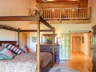Experience rustic charm in this spacious bedroom featuring a grand four-poster bed adorned with decorative pillows and a cozy comforter.