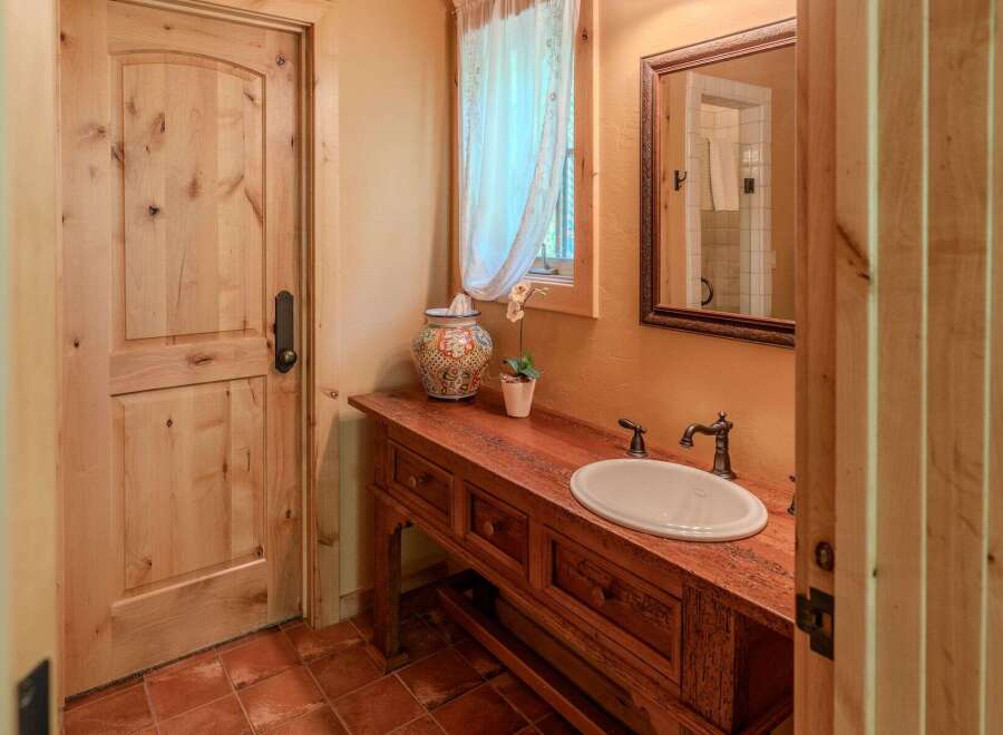 This charming bathroom features a rustic wooden vanity with a white oval sink and antique-style faucets.