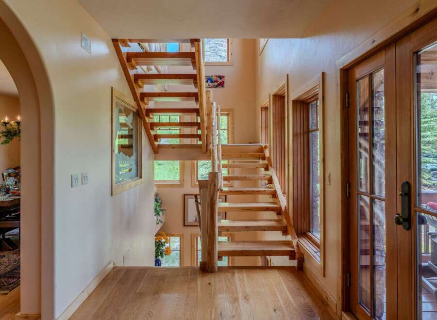 Experience rustic charm in this inviting entryway featuring a beautiful wooden staircase and natural light streaming through large windows.