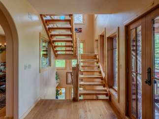 Experience rustic charm in this inviting entryway featuring a beautiful wooden staircase and natural light streaming through large windows.