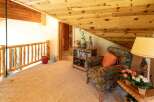 Experience rustic charm in this cozy loft space, featuring a natural wood railing and a warm, inviting armchair perfect for relaxation.