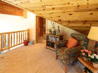 Experience rustic charm in this cozy loft space, featuring a natural wood railing and a warm, inviting armchair perfect for relaxation.