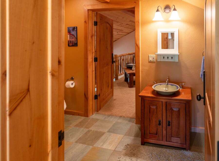 This charming bathroom features a rustic wooden vanity with a vessel sink, complemented by warm orange walls and natural wood accents.
