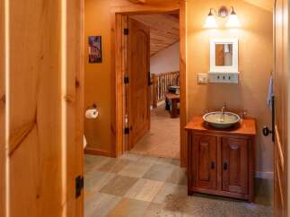 This charming bathroom features a rustic wooden vanity with a vessel sink, complemented by warm orange walls and natural wood accents.