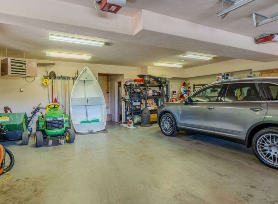 This spacious garage offers ample storage and parking solutions, featuring a large boat, a riding lawnmower, and a sleek SUV.