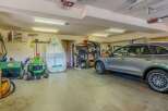 This spacious garage offers ample storage and parking solutions, featuring a large boat, a riding lawnmower, and a sleek SUV.
