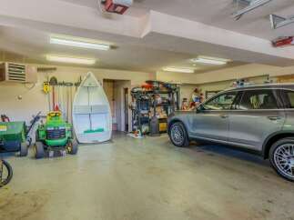 This spacious garage offers ample storage and parking solutions, featuring a large boat, a riding lawnmower, and a sleek SUV.