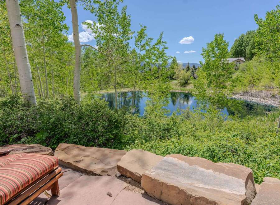 Escape to this serene oasis featuring a tranquil pond surrounded by lush greenery and mature aspen trees.