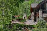 Enjoy the serene mountain lifestyle with this stunning outdoor living space, featuring a charming stone fireplace and comfortable seating under two large umbrellas.