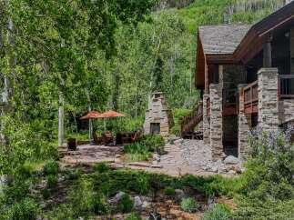 Enjoy the serene mountain lifestyle with this stunning outdoor living space, featuring a charming stone fireplace and comfortable seating under two large umbrellas.