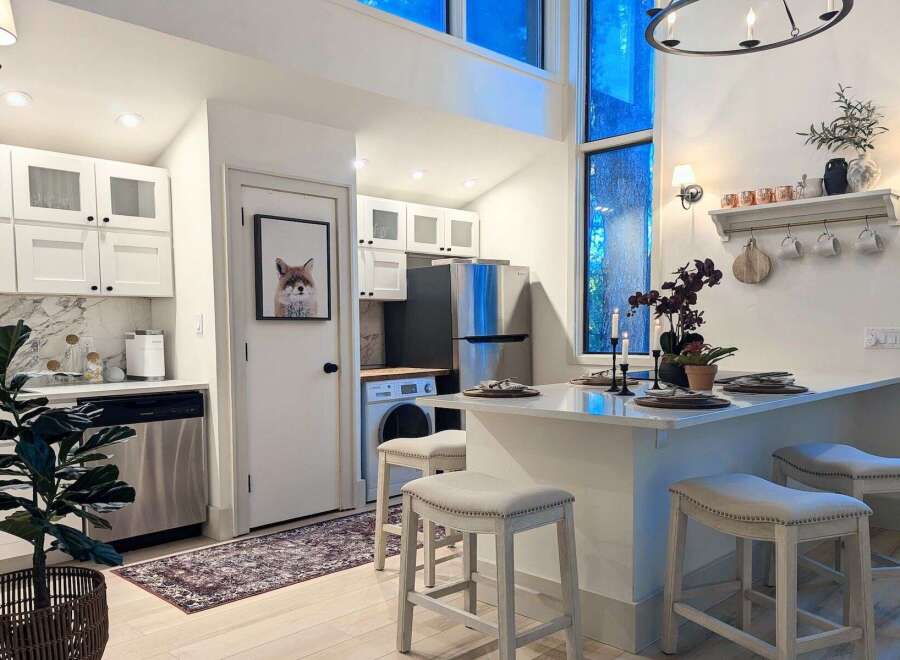 This modern kitchen features sleek white cabinetry, a marble backsplash, and stainless steel appliances, creating a bright and functional space.